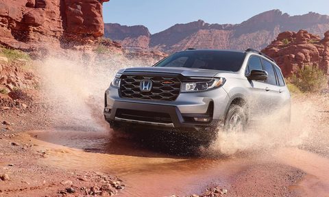 Front view of Honda's 2025 Passport TrailSport splashing through a puddle in the backcountry.