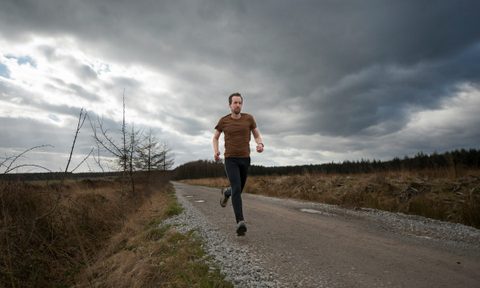 man running outside grey clouds on road