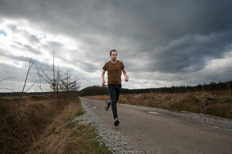 man running outside grey clouds on road