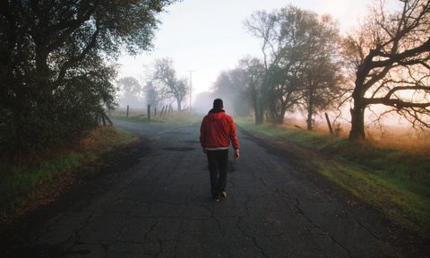 man walking with red jacket on road outdoors tree