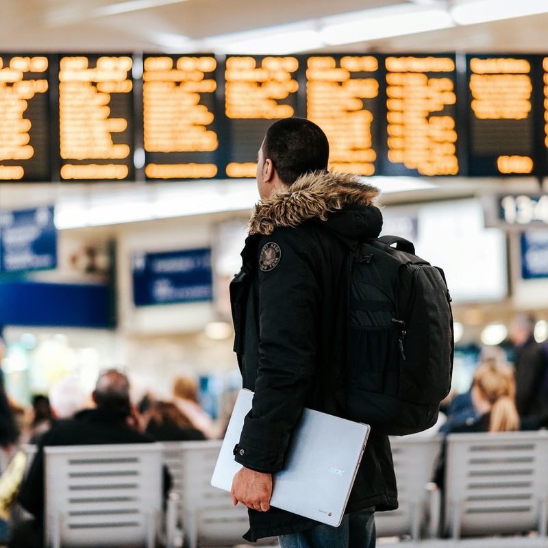 man standing in airport looking at flight schedule