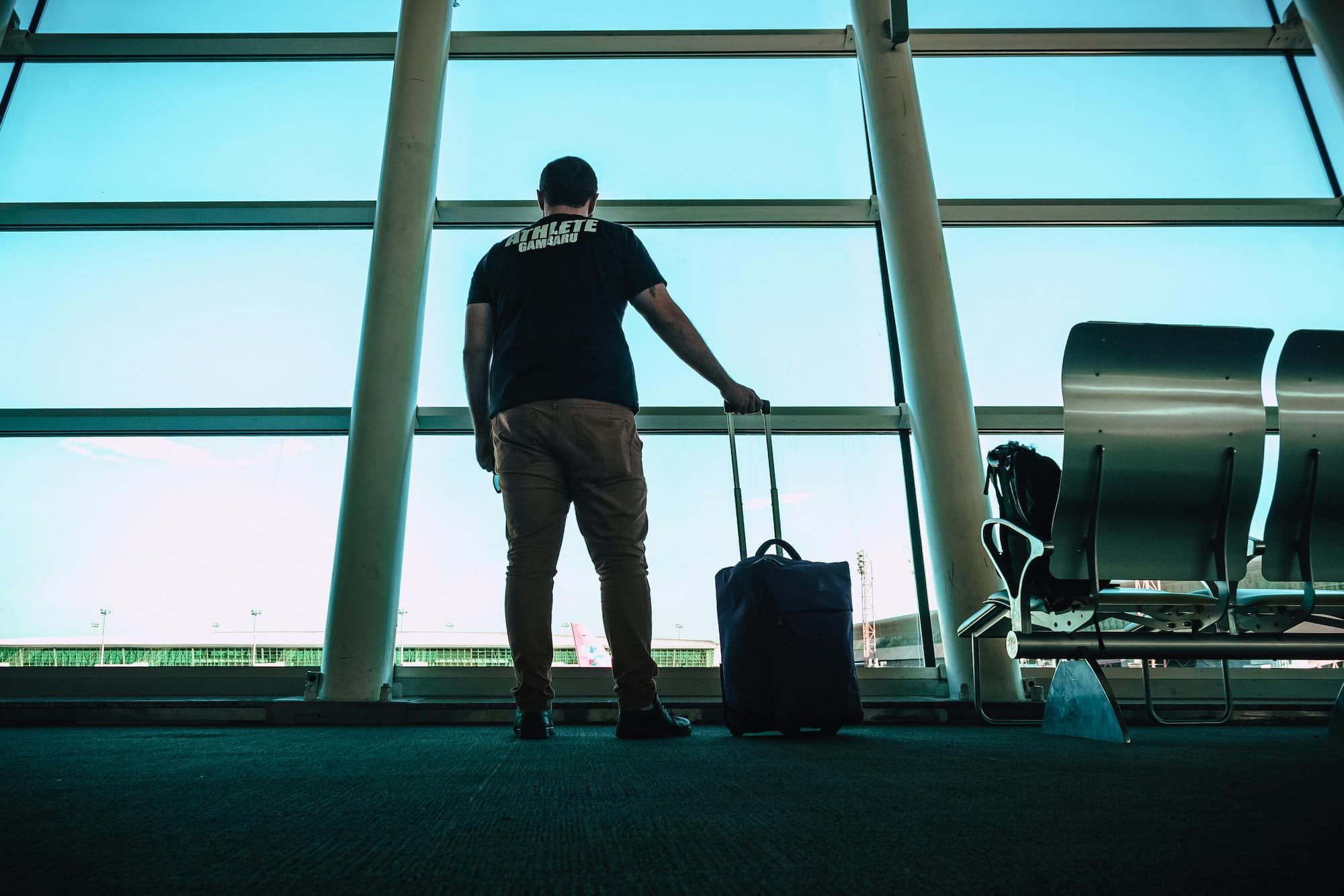man in airport with rolling suitcase in hand