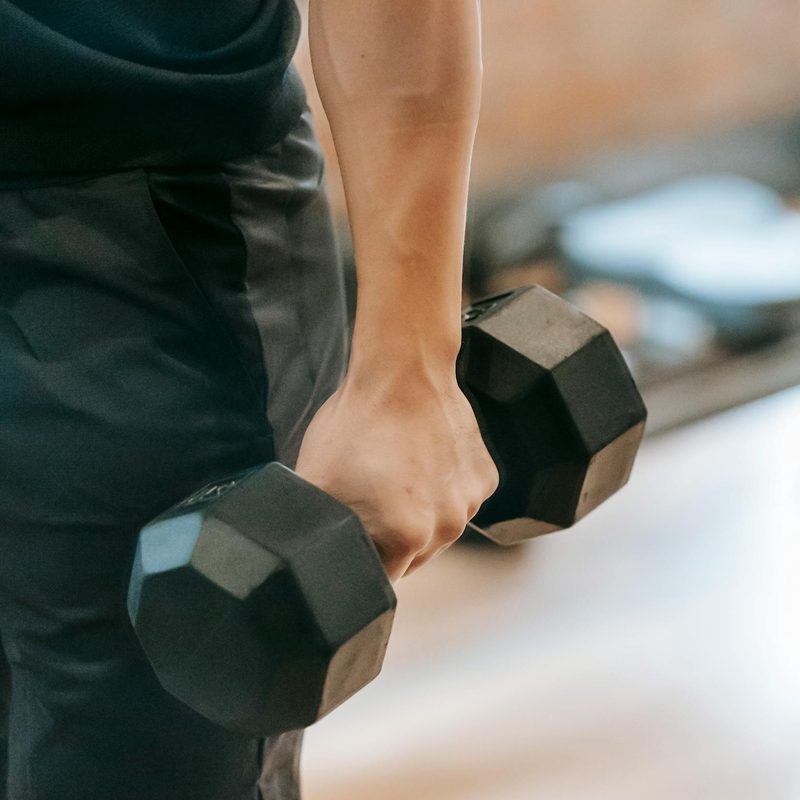 man holding dumbbell arms down by side close up dumbbell shrug