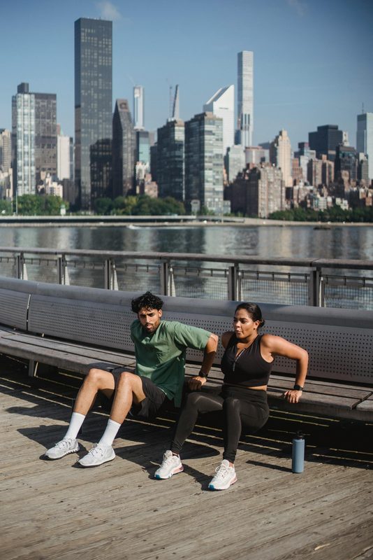 man and woman outside doing bench dip by water