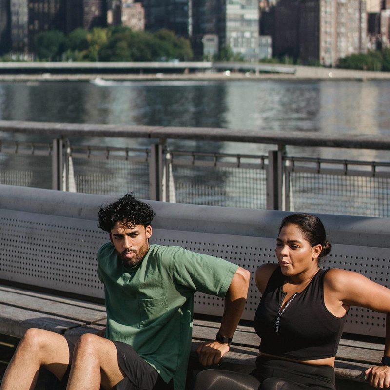Man and woman outside doing bench dip by water