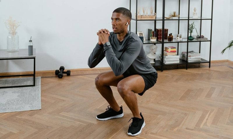 Man squatting down doing jump squats at home workout