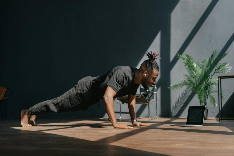 Man working with remote personal trainer doing virtual exercise class at home working out yoga plank pushup