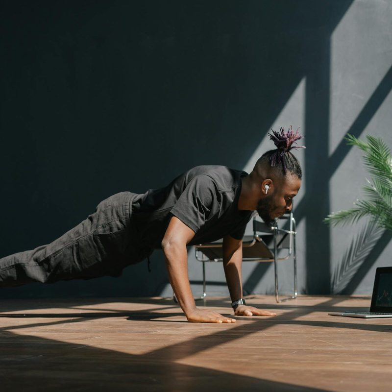 Man working with remote personal trainer doing virtual exercise class at home working out yoga plank pushup