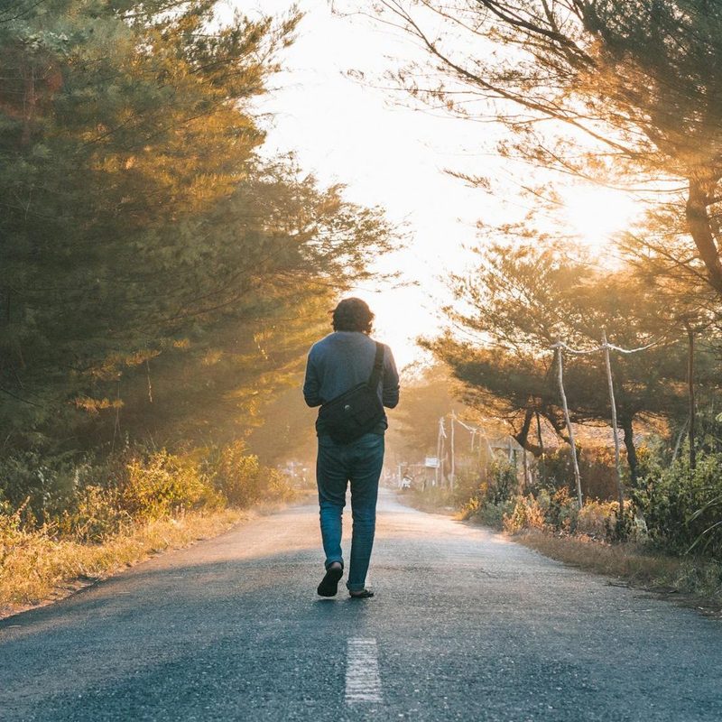 Man walking outdoors through sunlit road trees