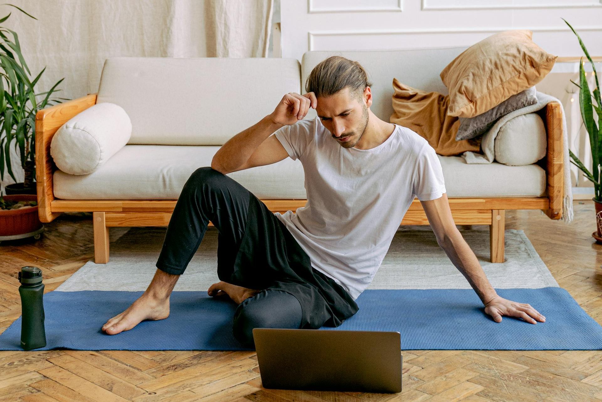 man sitting on yoga mat at home workout laptop exercise class thinking