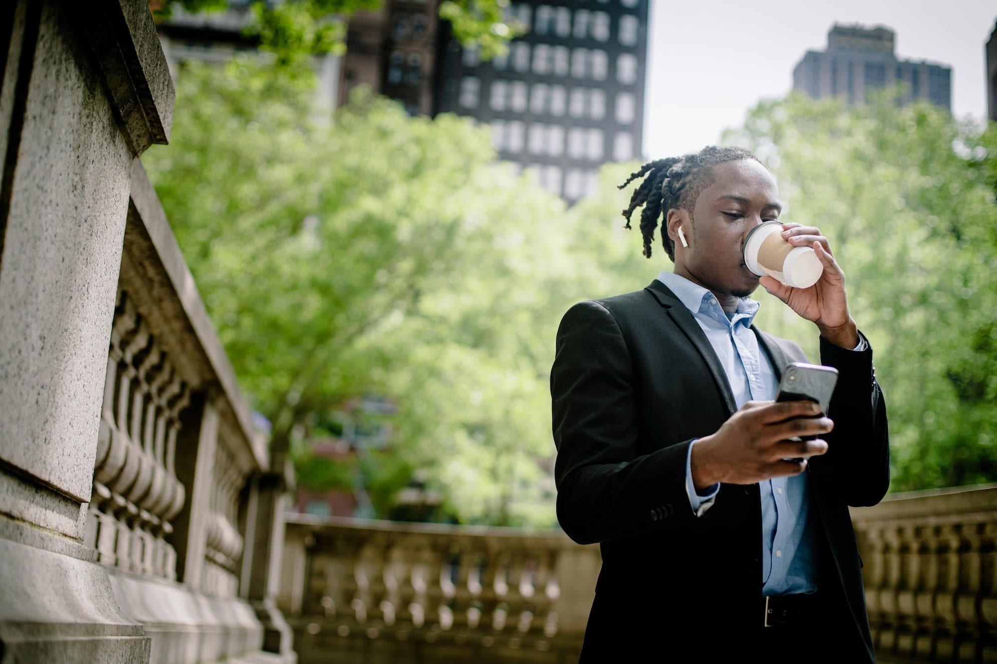 man outside drinking coffee while looking at his phone