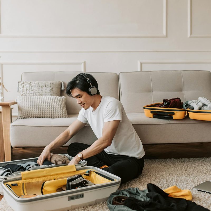 a man wearing headphones while packing clothes in a suitcase