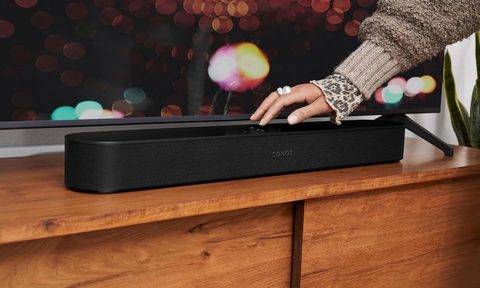 A woman touches a Sonos Beam 2 that is below her TV.