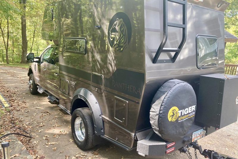 Rear view of Tiger Adventure Vehicles' Panthera off-road truck camper parked in the woods.