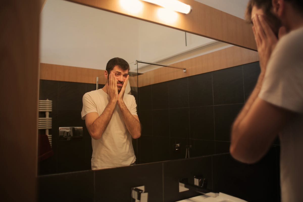 tired man white t-shirt looking in mirror