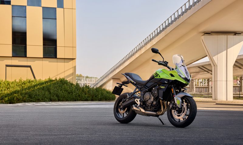 2025 Triumph Tiger Sport 660 right front three-quarter view parked on asphalt near an office building and highway overpass.