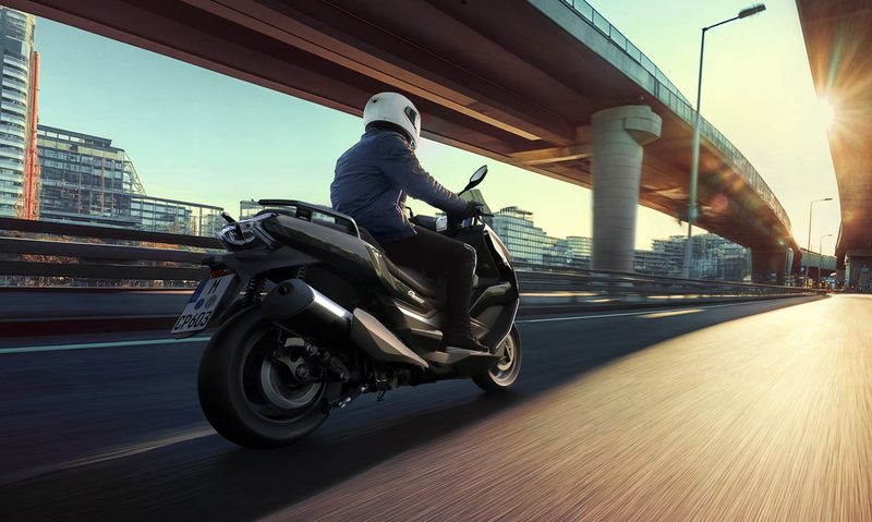 Single rider on a 2025 BMW C 400 GT on a highway through a city right rear three-quarter view.