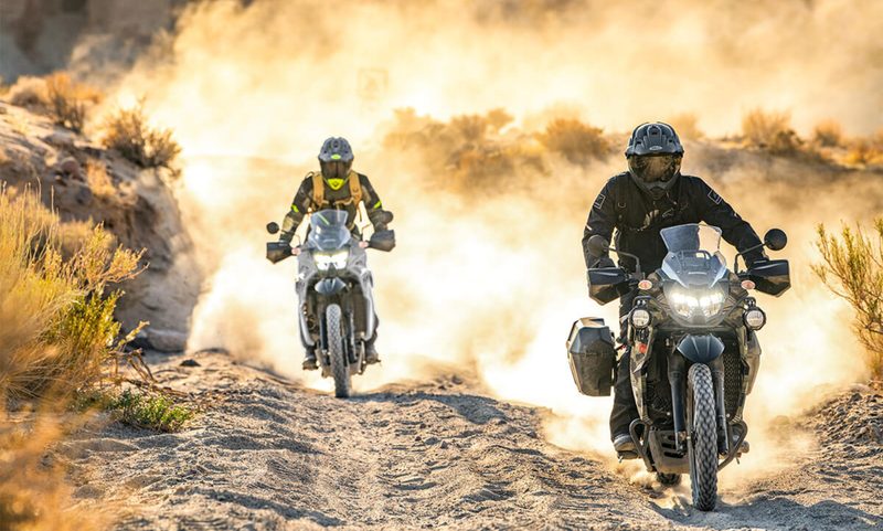 Two riders on 2025 Kawasaki KLR 650 Aadventure ABS riding on dirt roads with a lot of dust.
