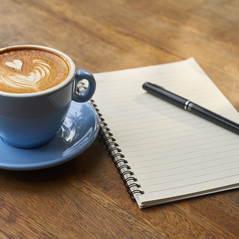 Latte next to a pad of paper and a pen