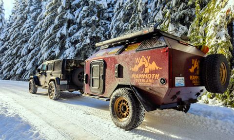 A WLY Mammoth camper/trailer being towed up a snowy treelined road.