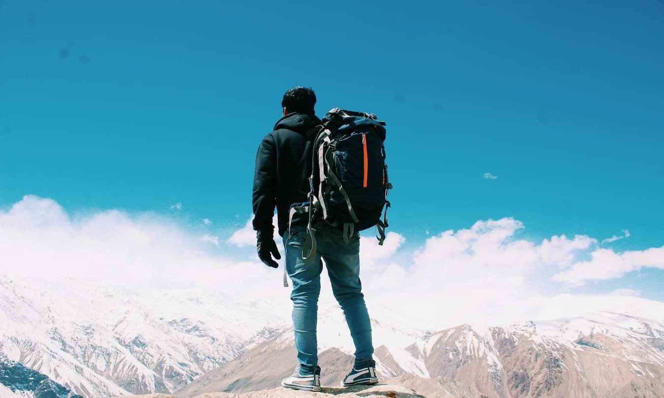 man wearing a duffel bag as a backpack standing outside looking at mountains
