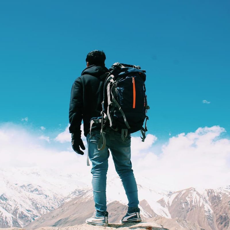 Man wearing a duffel bag as a backpack standing outside looking at mountains