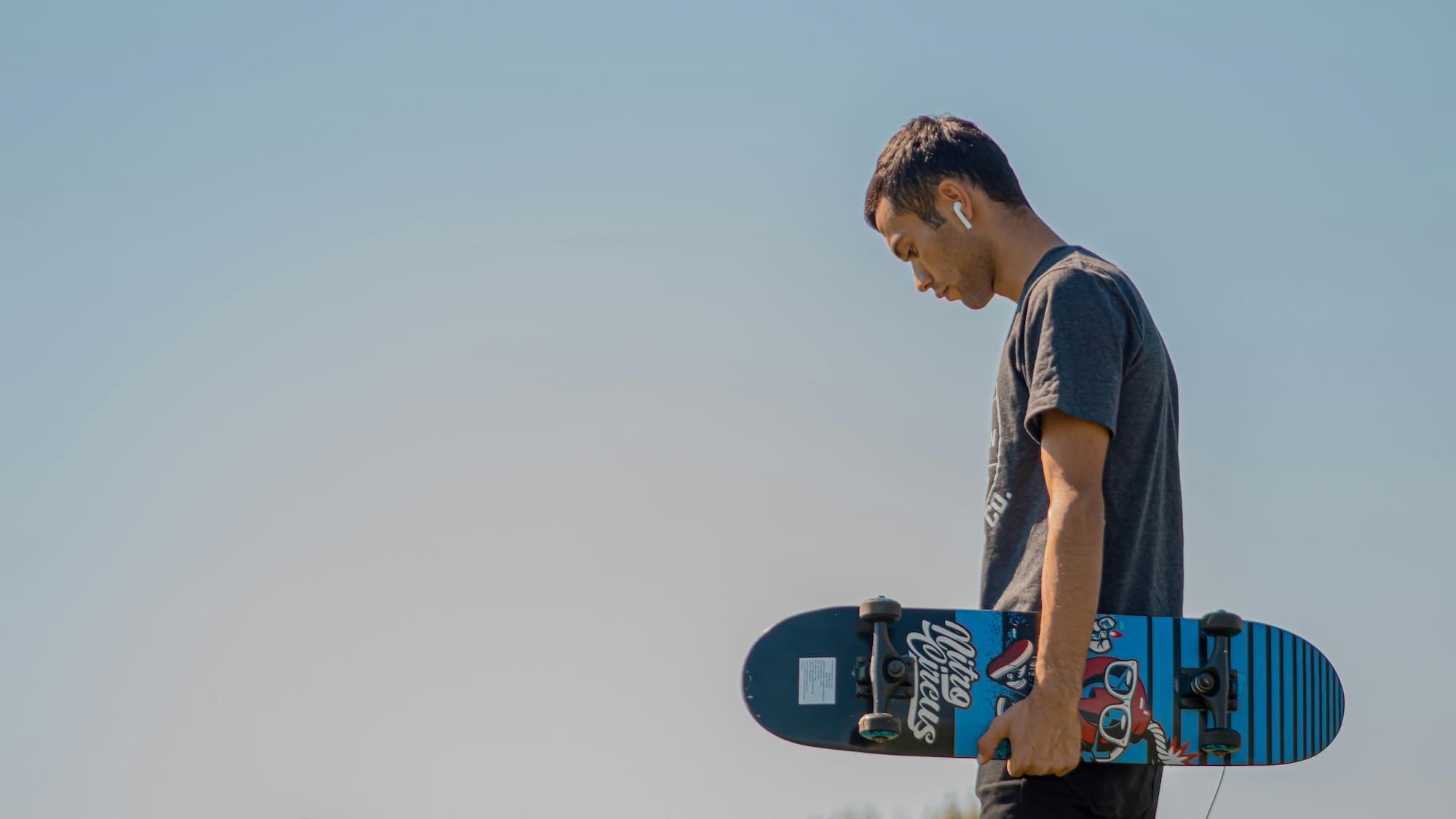 man holding a skateboard outside with airpods in his ears
