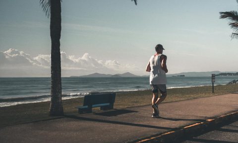 Man jogging outside by water and a palm tree