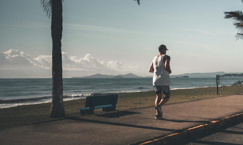 Man jogging outside by water and a palm tree