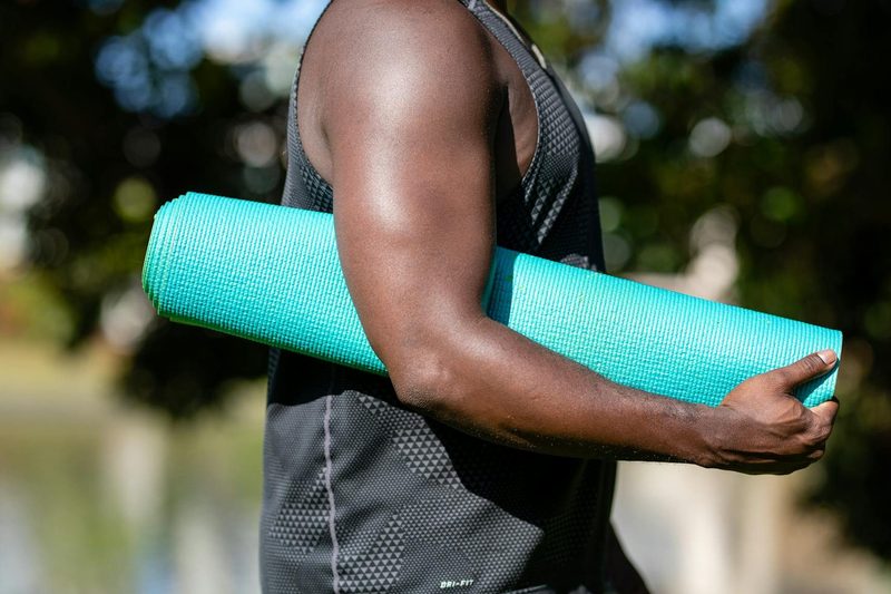 Man with strong arm muscles holding a blue yoga mat outdoors