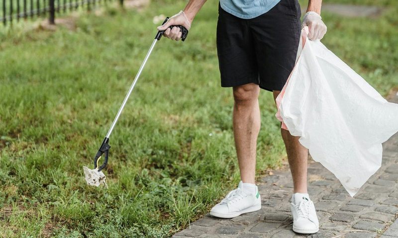 Man with trash picker plogging picking up rubbish outside on gras