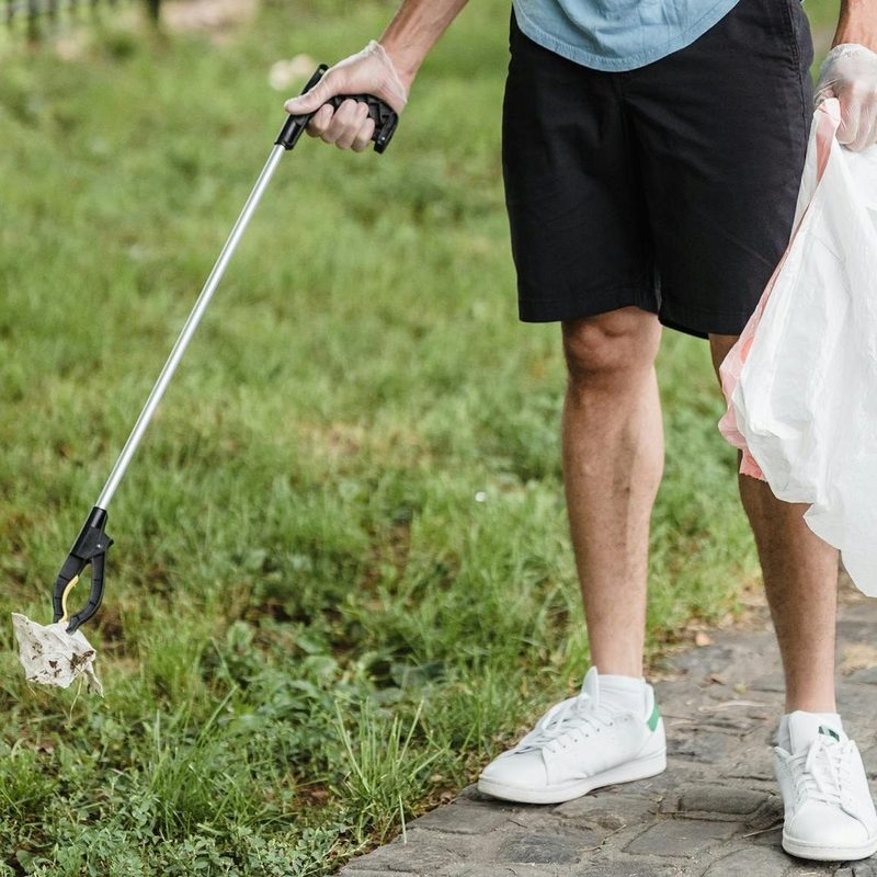 Man with trash picker plogging picking up rubbish outside on gras