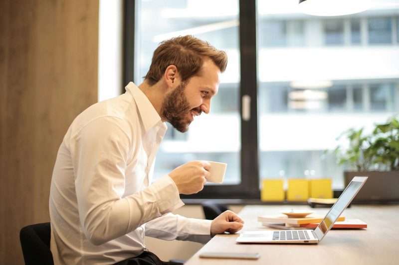 man smiling drinking tea working at desk