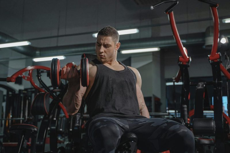 Man doing bicep curl in gym - one arm unilateral with a dumbbell
