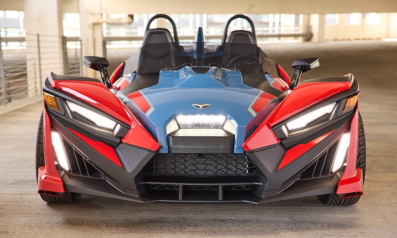 2025 Polaris Slingshot SLR driving by a river and bridge.