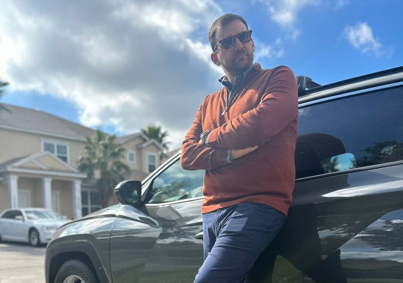Man leaning on car in orange sweater