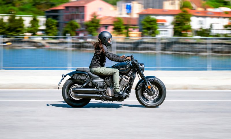 Person riding a 2025 Benda Chinchilla 500 on a bridge with a river and small businesses in the background.
