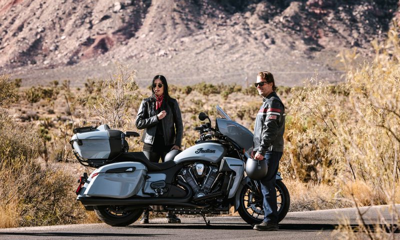 Two people standing on the side of the road next to a 2025 Indian Roadmaster PowerPlus with desert in the background.