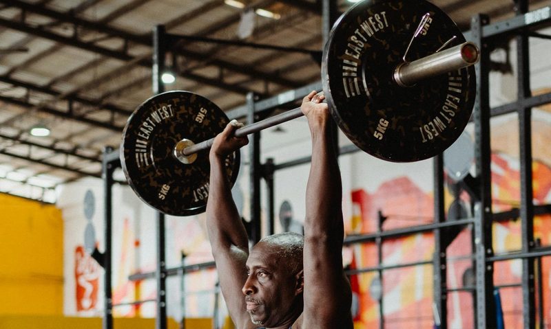 man lifting overhead barbell press in gym