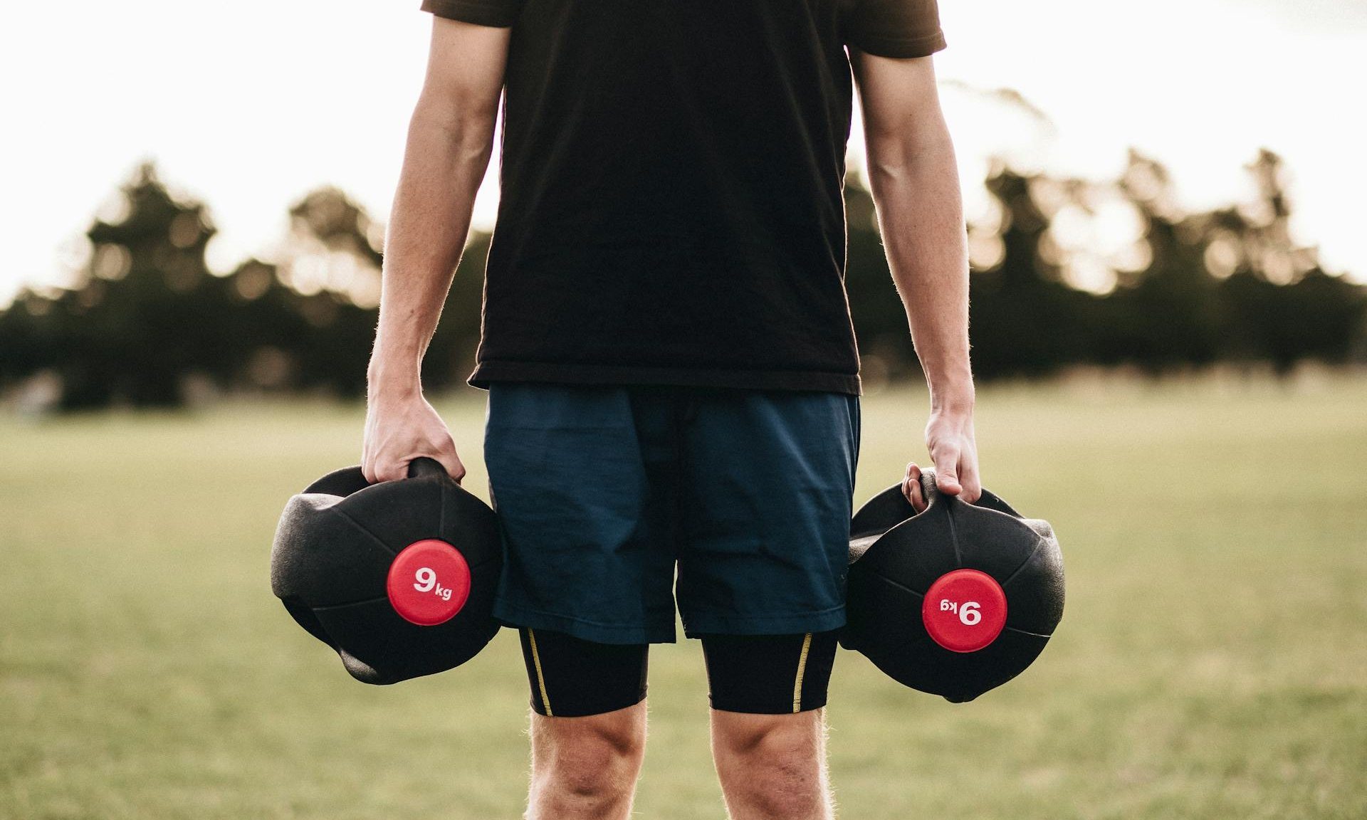 man outside on grass holding weights dumbbells