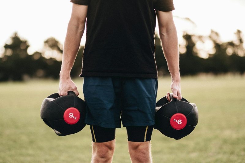 man outside on grass holding weights dumbbells