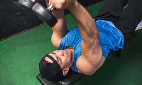 Man doing skull crushers exercise with dumbbells close up on bench