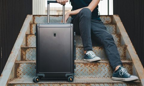 Person sitting on stairs with a black rolling suitcase