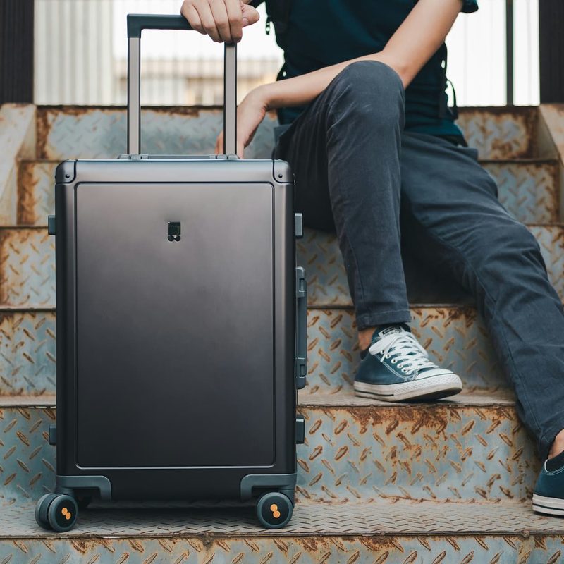 person sitting on stairs with a black rolling suitcase