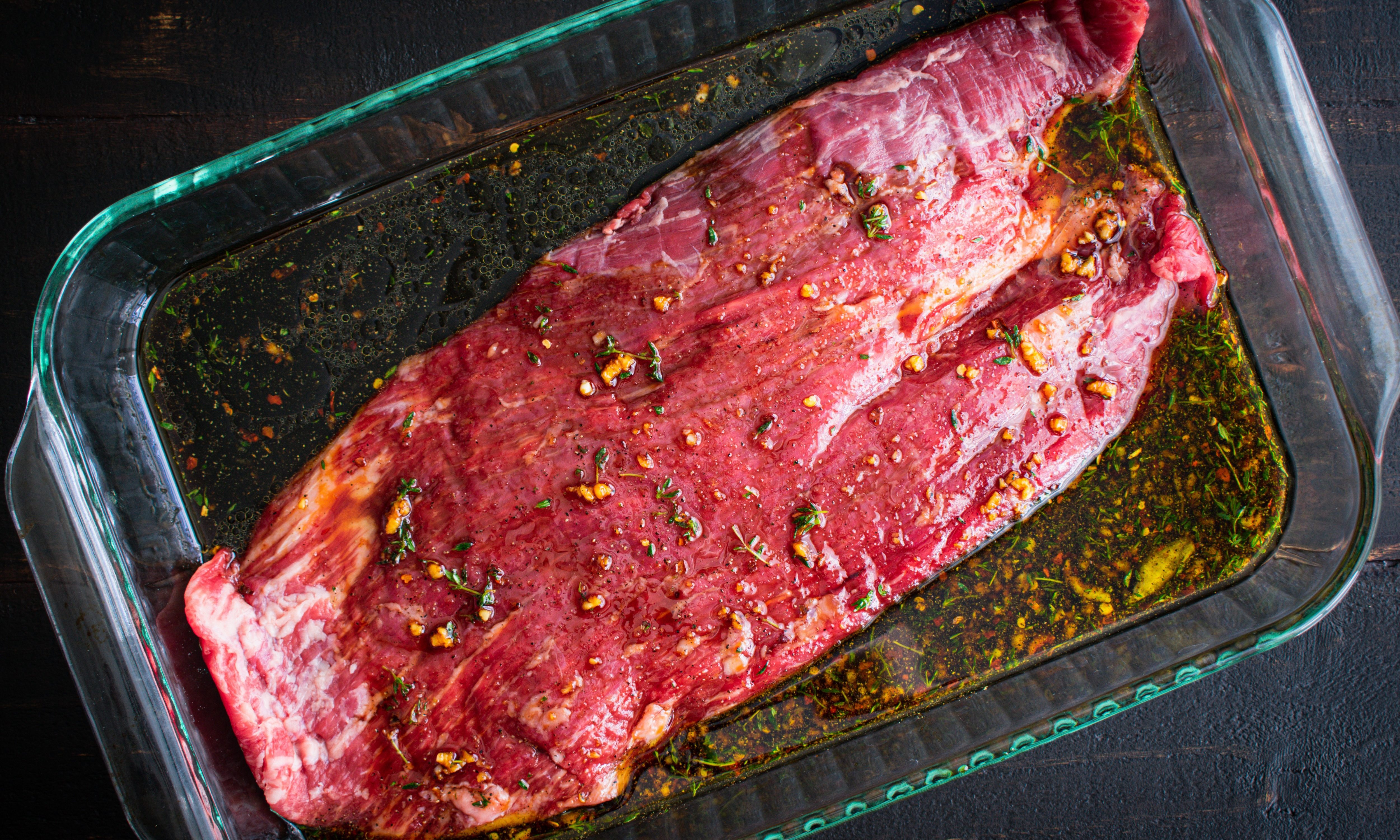 Marinating Flank Steak in a Glass Dish: A raw flank steak marinating in a glass baking dish