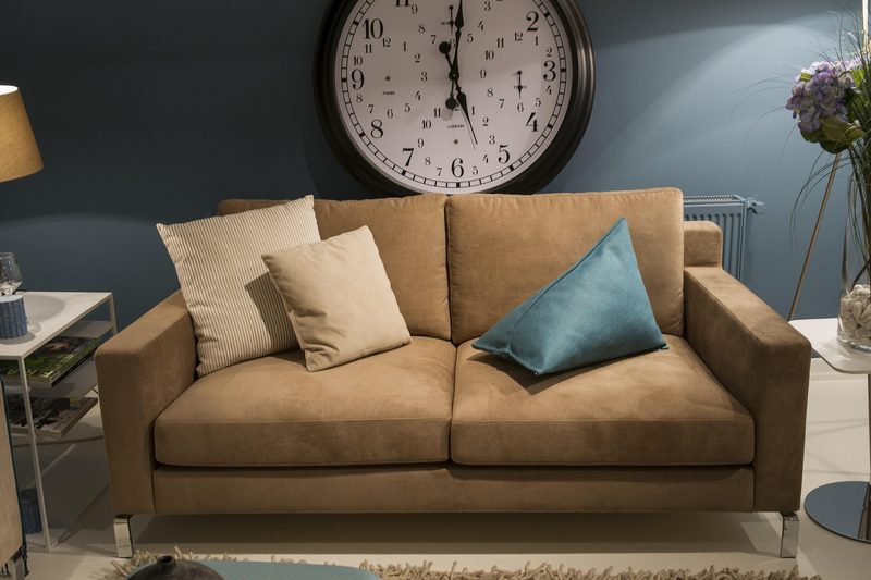 A large clock on the wall and a couch with pillows inside a home