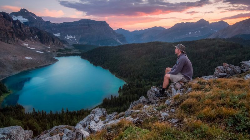 A man hiking to a beautiful view of a lake at sunset