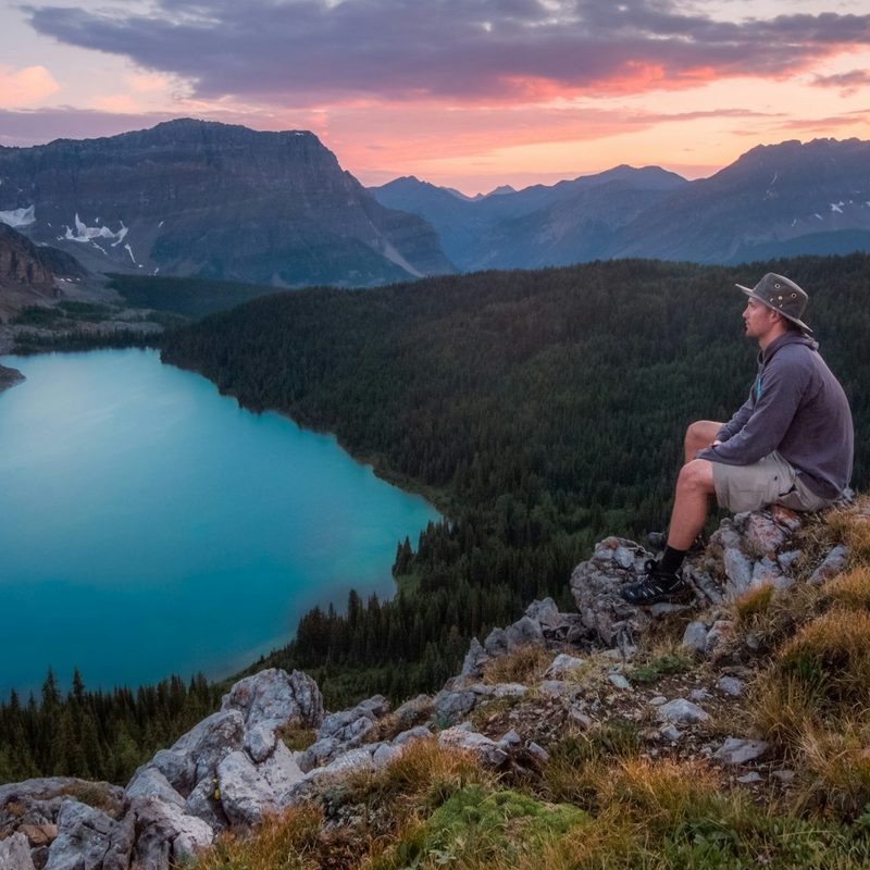 A man hiking to a beautiful view of a lake at sunset