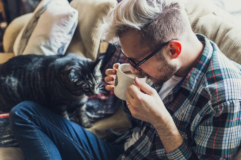 Man drinking coffee sitting relaxing on couch with cat