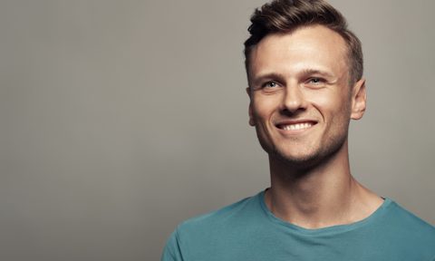Male beauty concept. Portrait of smiling 30-year-old man standing in blue t-shirt over gray background . Close up. Classic style. Wavy glossy blond hair. Studio shot